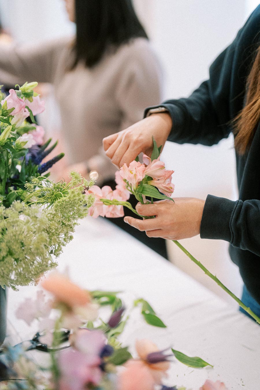 Person arranging a bouquet with pink and white flowers on a table, showcasing creative floral design skills in a workshop setting.