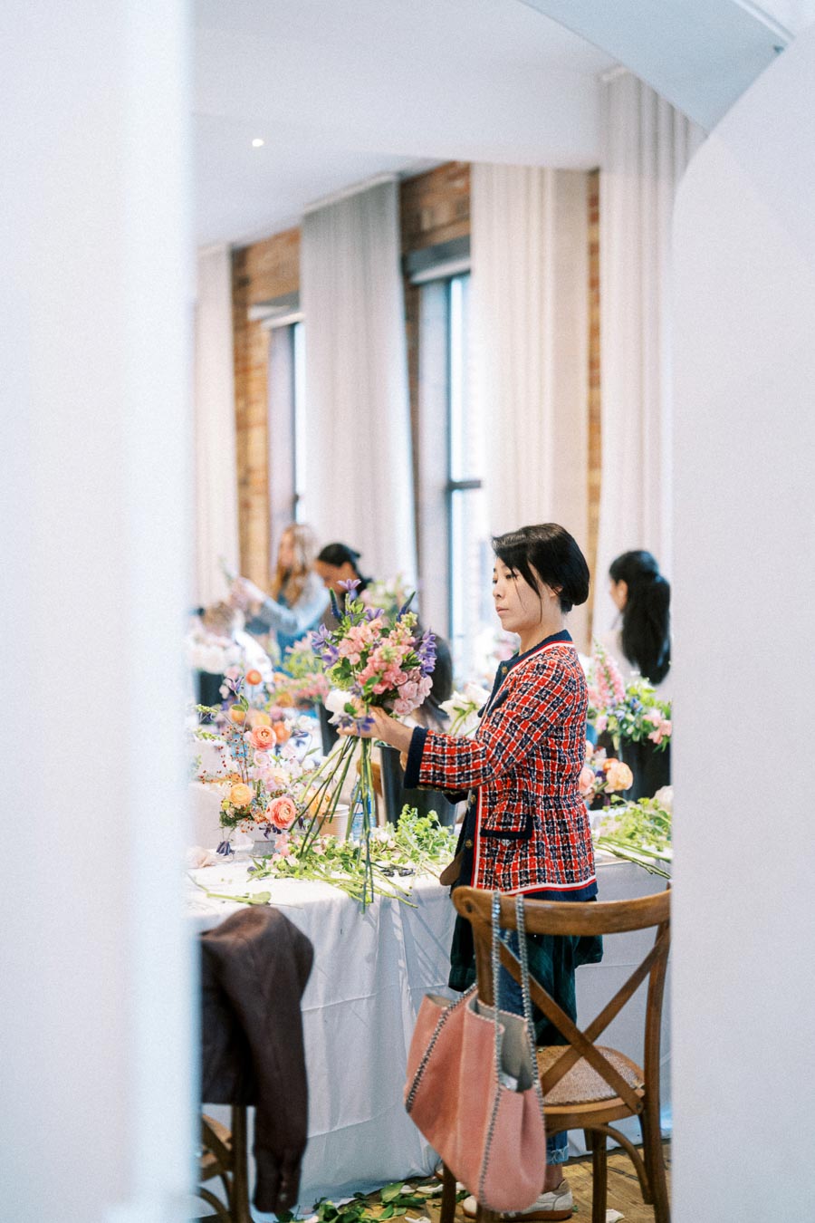 Person arranging a vibrant flower bouquet in a well-lit workshop setting, surrounded by colorful floral decorations and wooden furniture.