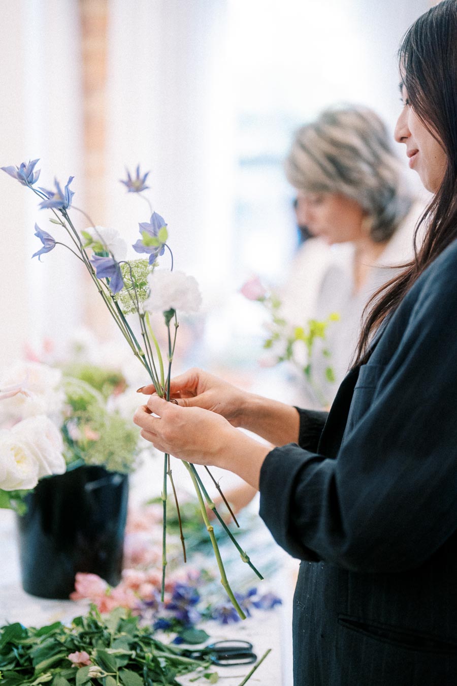 Florist arranging a bouquet of purple and white flowers in a workshop setting, focusing on creativity and floral design process.
