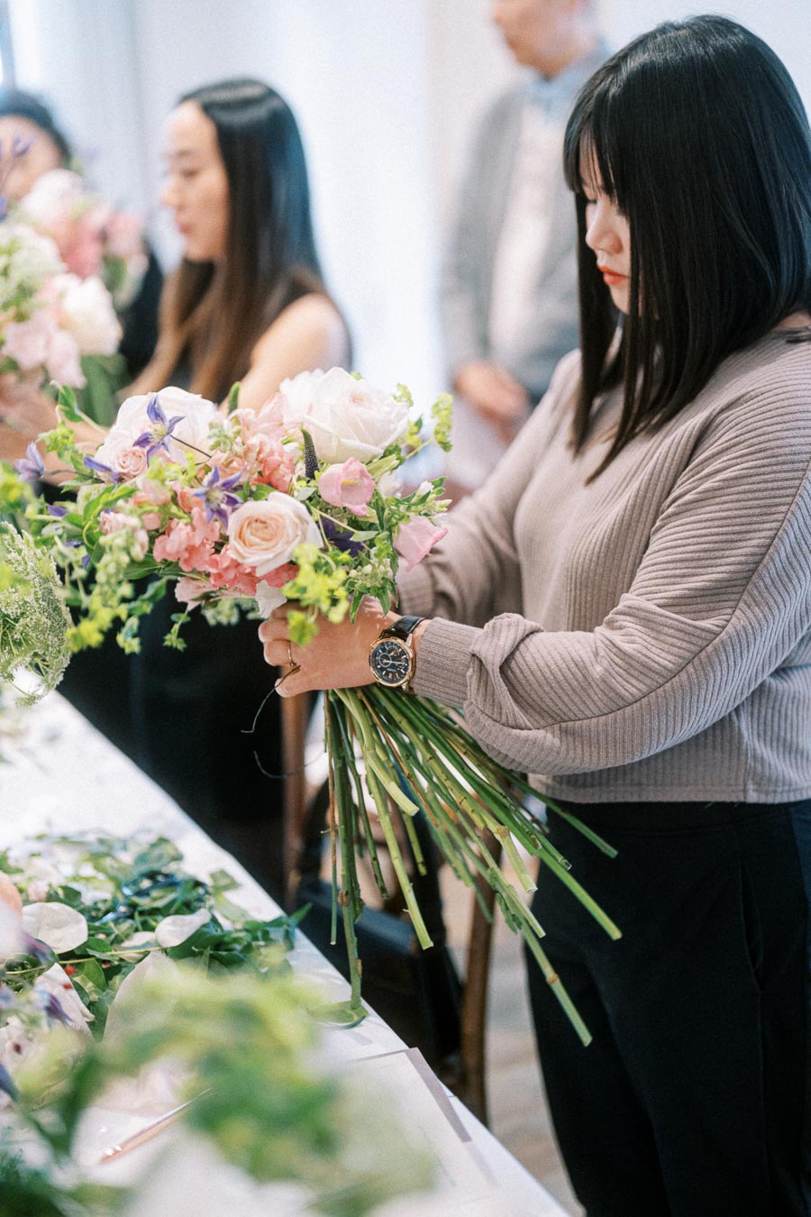 A woman arranging a bouquet of fresh pink and white flowers with greenery during a floral workshop.
