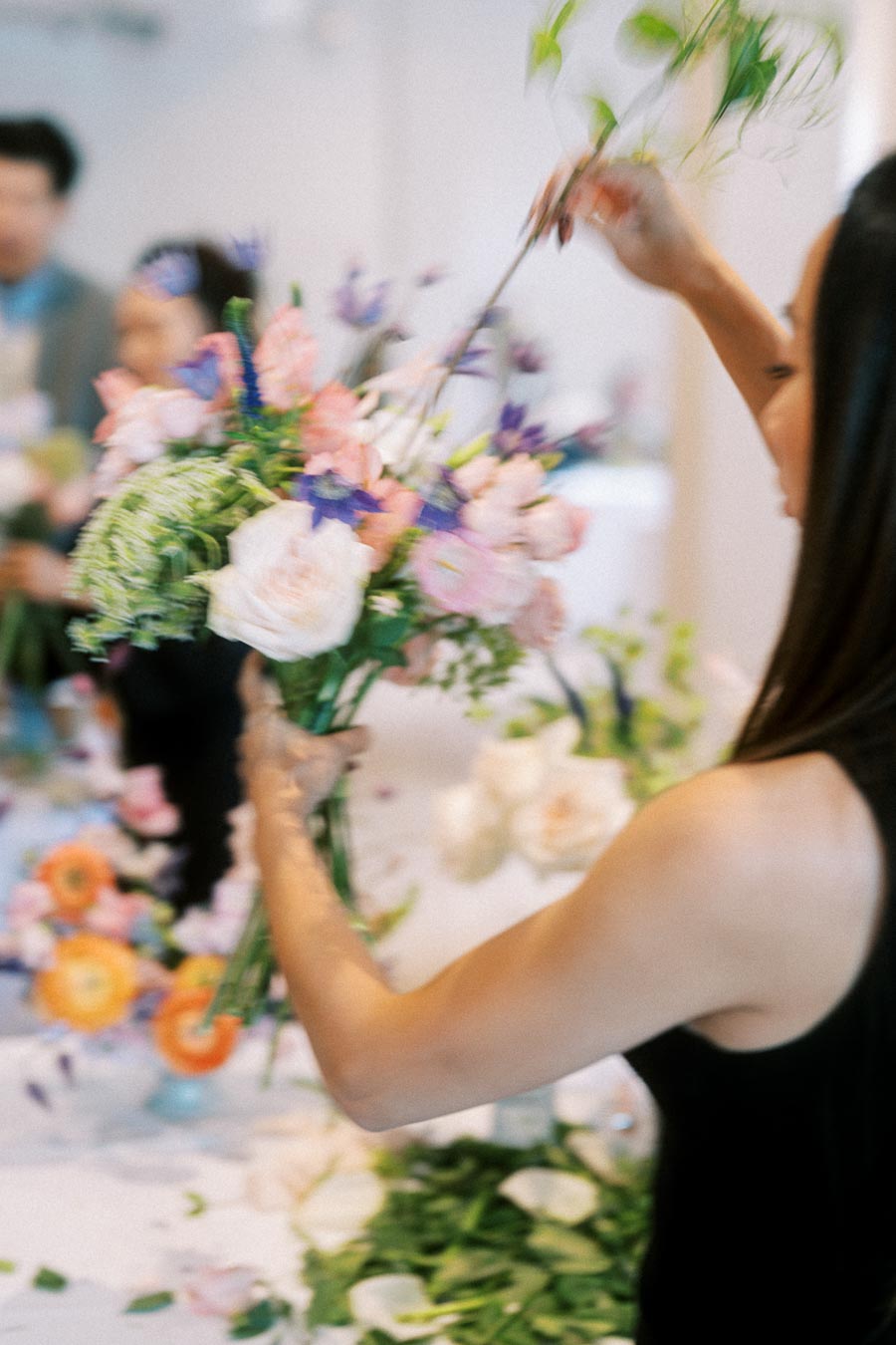 Florist arranging a vibrant bouquet of pink, purple, and cream flowers during a floral design workshop.