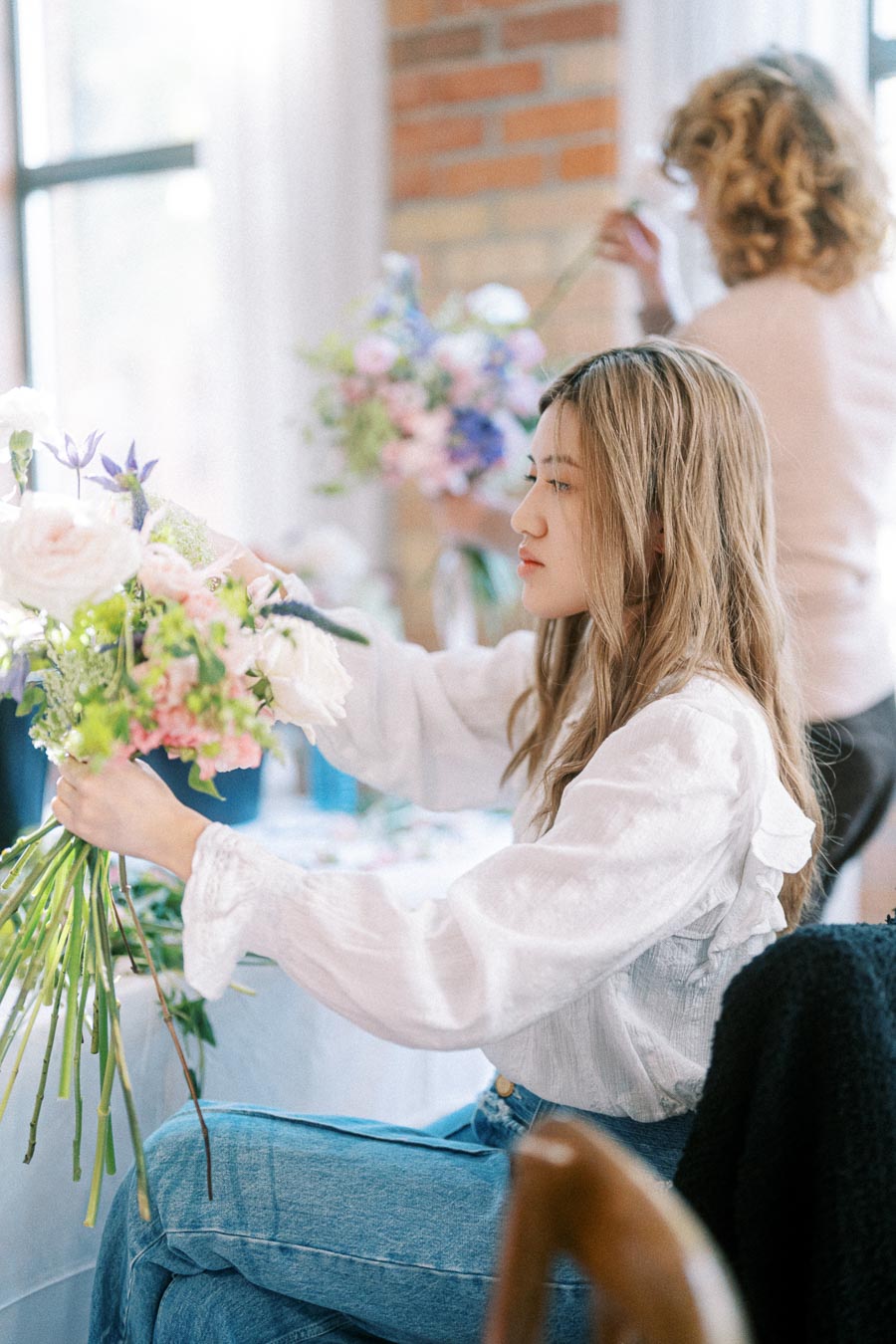 Young woman arranging a vibrant bouquet of flowers in a bright, airy room, focusing on creating a visually appealing floral design.