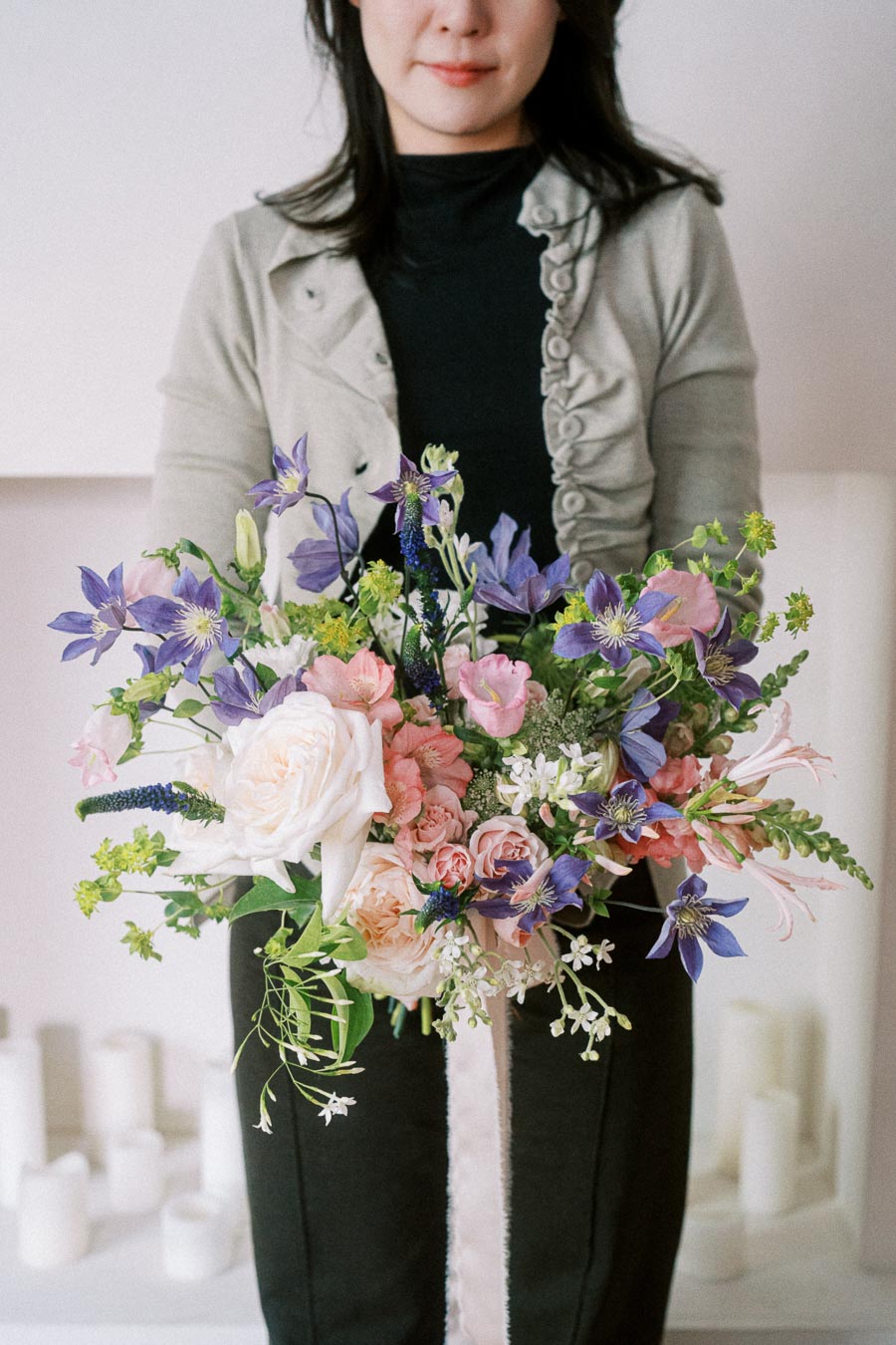Elegant woman holding a vibrant bouquet with purple, pink, and white flowers, showcasing a chic floral arrangement.