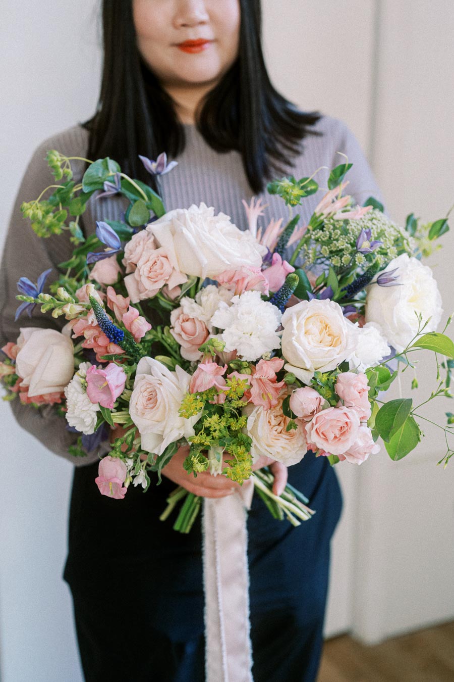 Person holding a beautiful bouquet of mixed flowers including roses and greenery, emphasizing soft pink and white tones.
