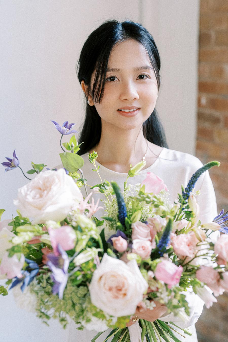 A person holding a beautiful bouquet of mixed flowers, including roses and various wildflowers, in a bright and elegant indoor setting.