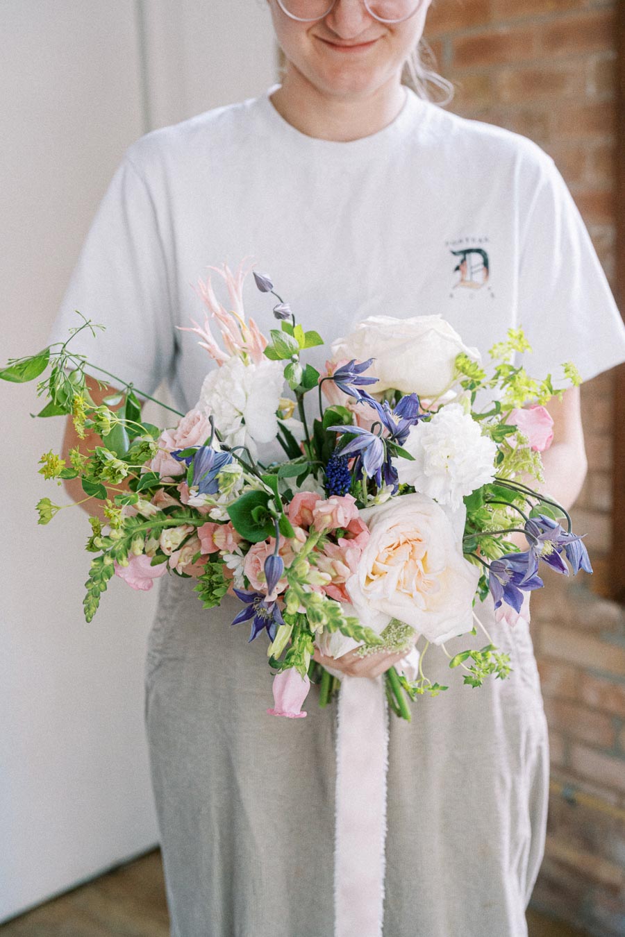 Person in a white shirt holding a colorful bouquet of fresh flowers including roses, lisianthus, and greenery, perfect for weddings and special occasions.