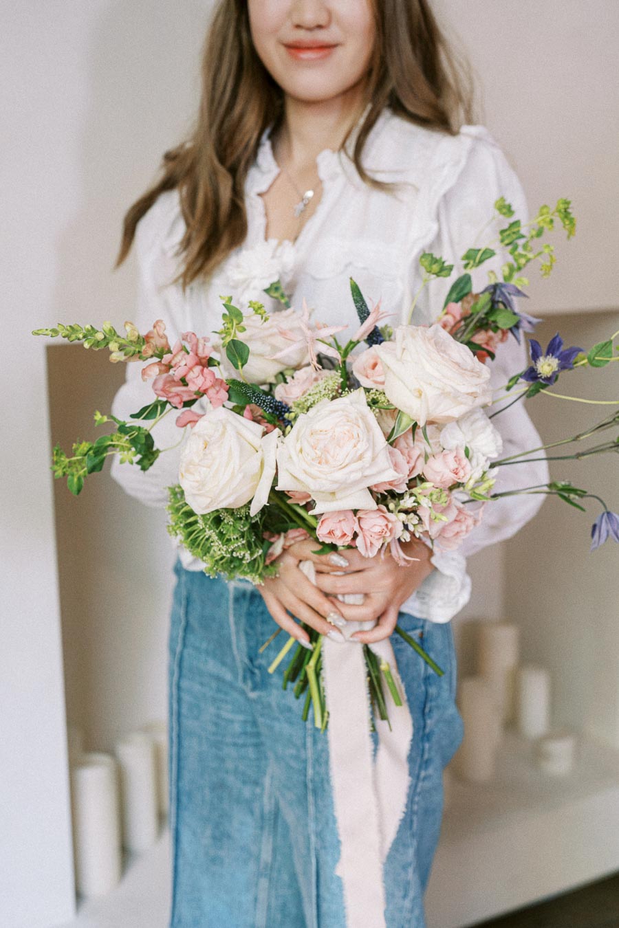 Young woman in a white blouse holding a beautiful bouquet of pink and white roses with greenery, showcasing a delicate floral arrangement ideal for weddings or special occasions.