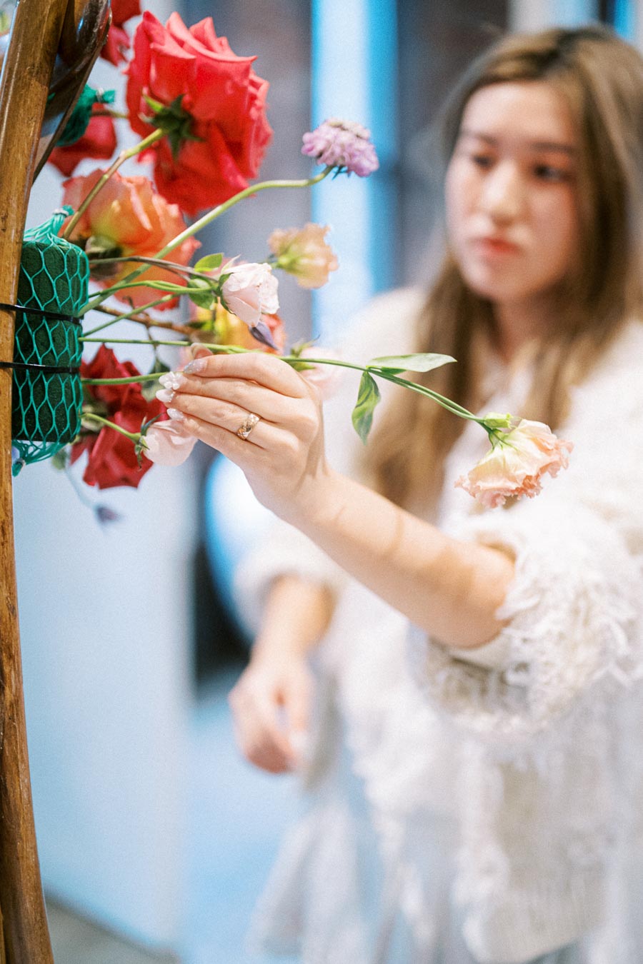 A florist arranging a vibrant bouquet of red and pink flowers in a floral shop.