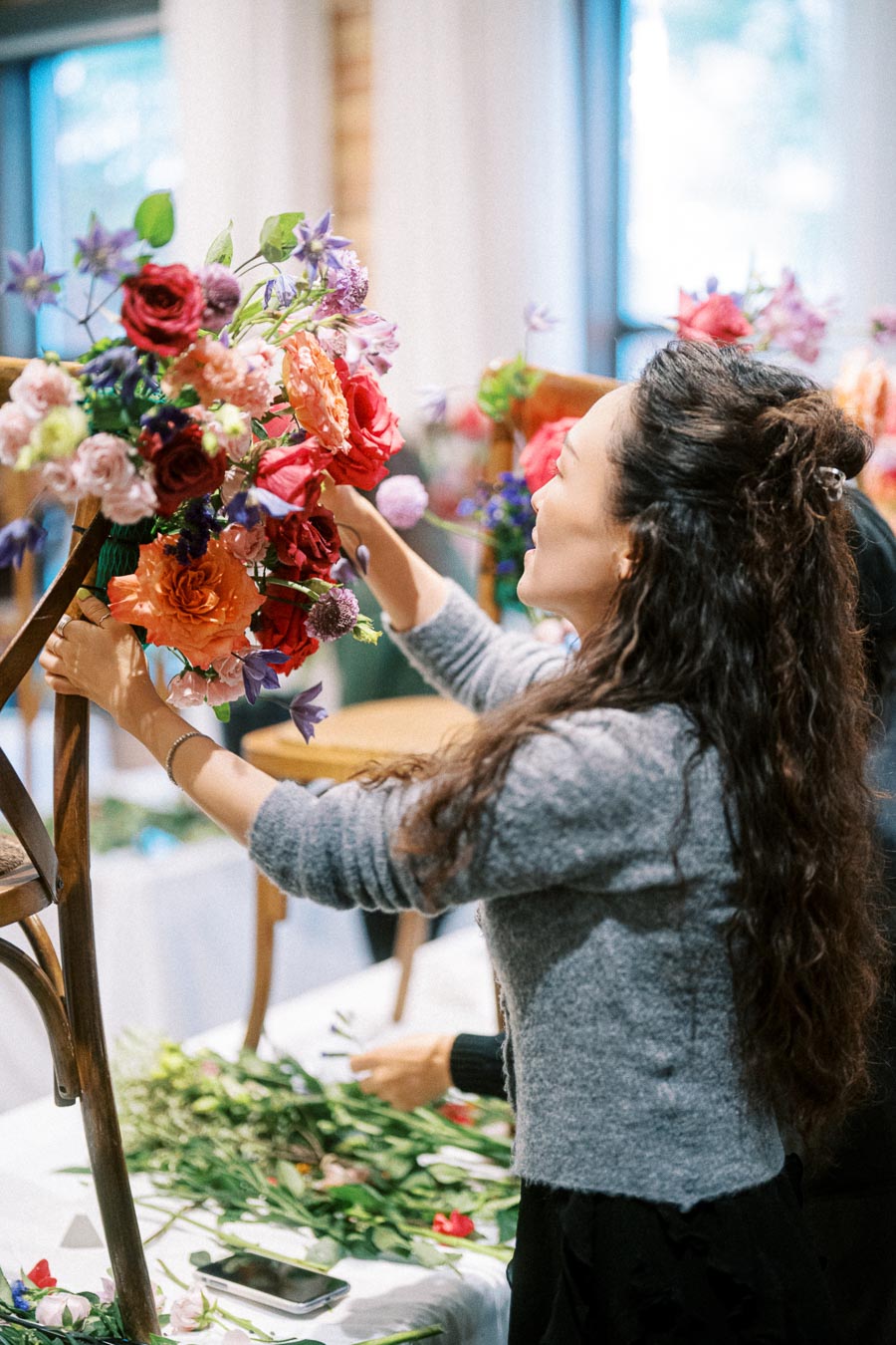 A woman arranging a vibrant floral display at an indoor event, showcasing colorful roses and various flowers.