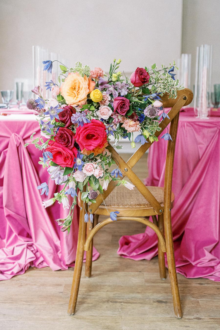 Elegant wooden chair with vibrant flower arrangement featuring roses and wildflowers, set against a pink draped table background, ideal for weddings or events.