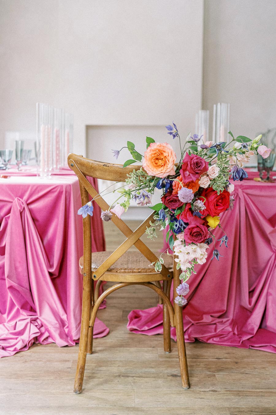 Rustic wooden chair adorned with vibrant floral arrangement, set against an elegantly draped pink tablecloth at a stylish wedding reception.