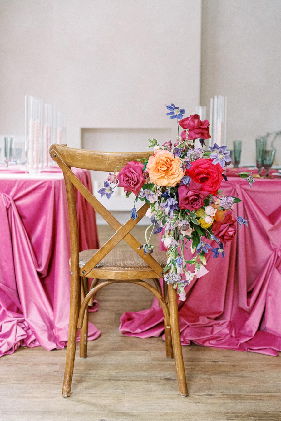Elegant wedding chair with colorful floral arrangement against a vibrant pink table setting.
