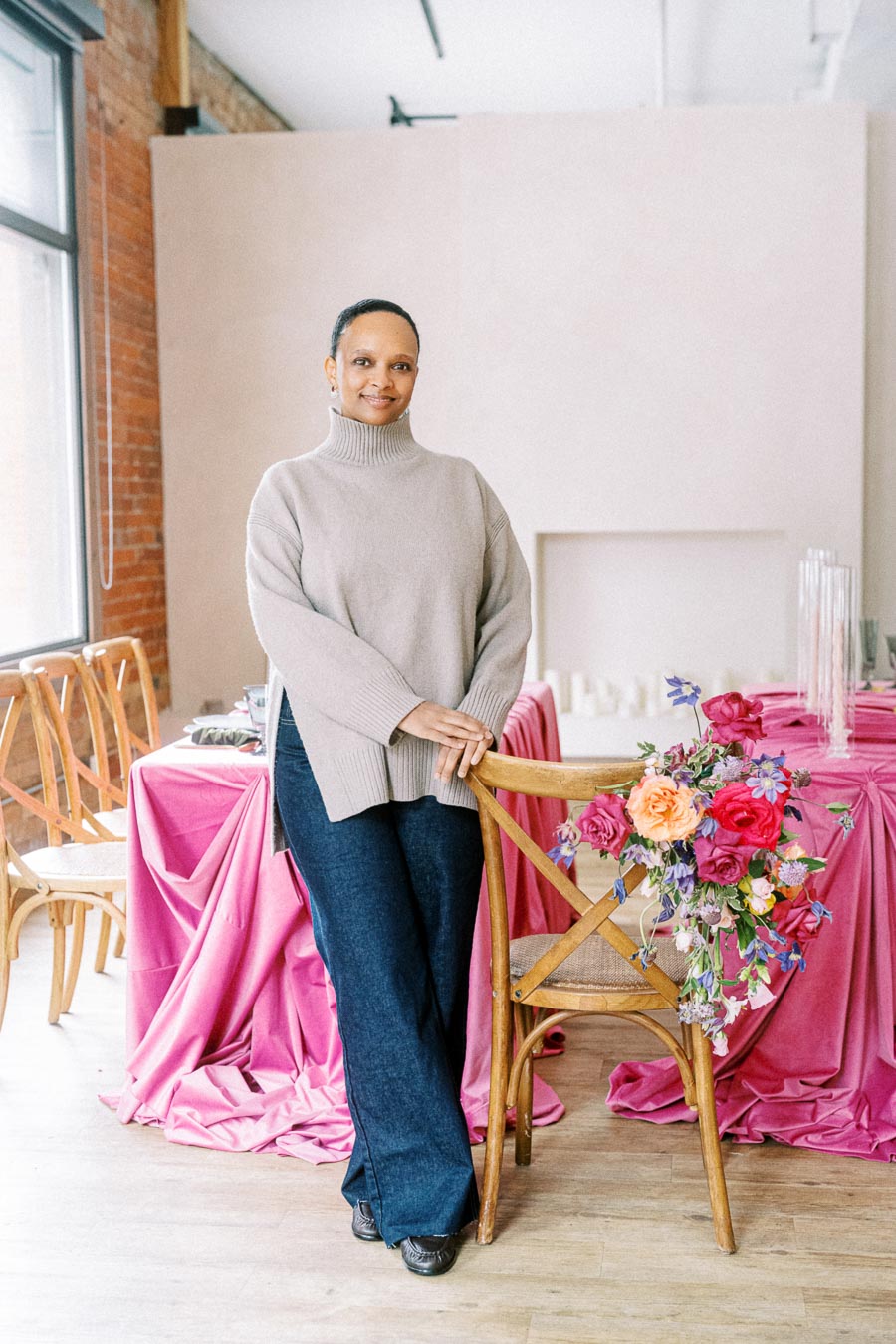 A person standing in a modern event space with pink tablecloths and floral decorations, showcasing stylish interior design elements and natural lighting.
