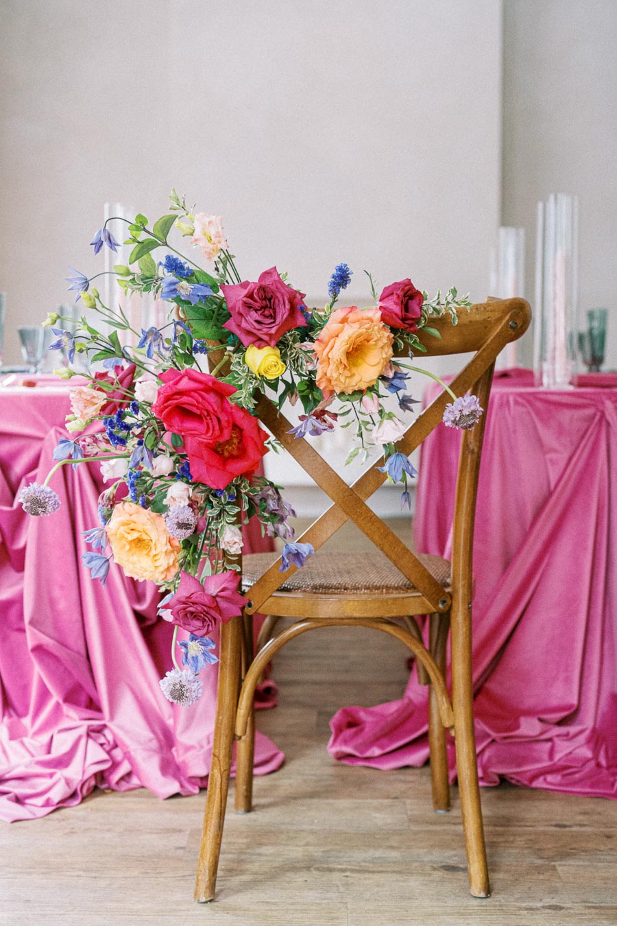 Wooden chair decorated with vibrant flowers, including red, pink, and yellow blooms, placed at a table with a pink draped tablecloth in a bright, elegant setting.