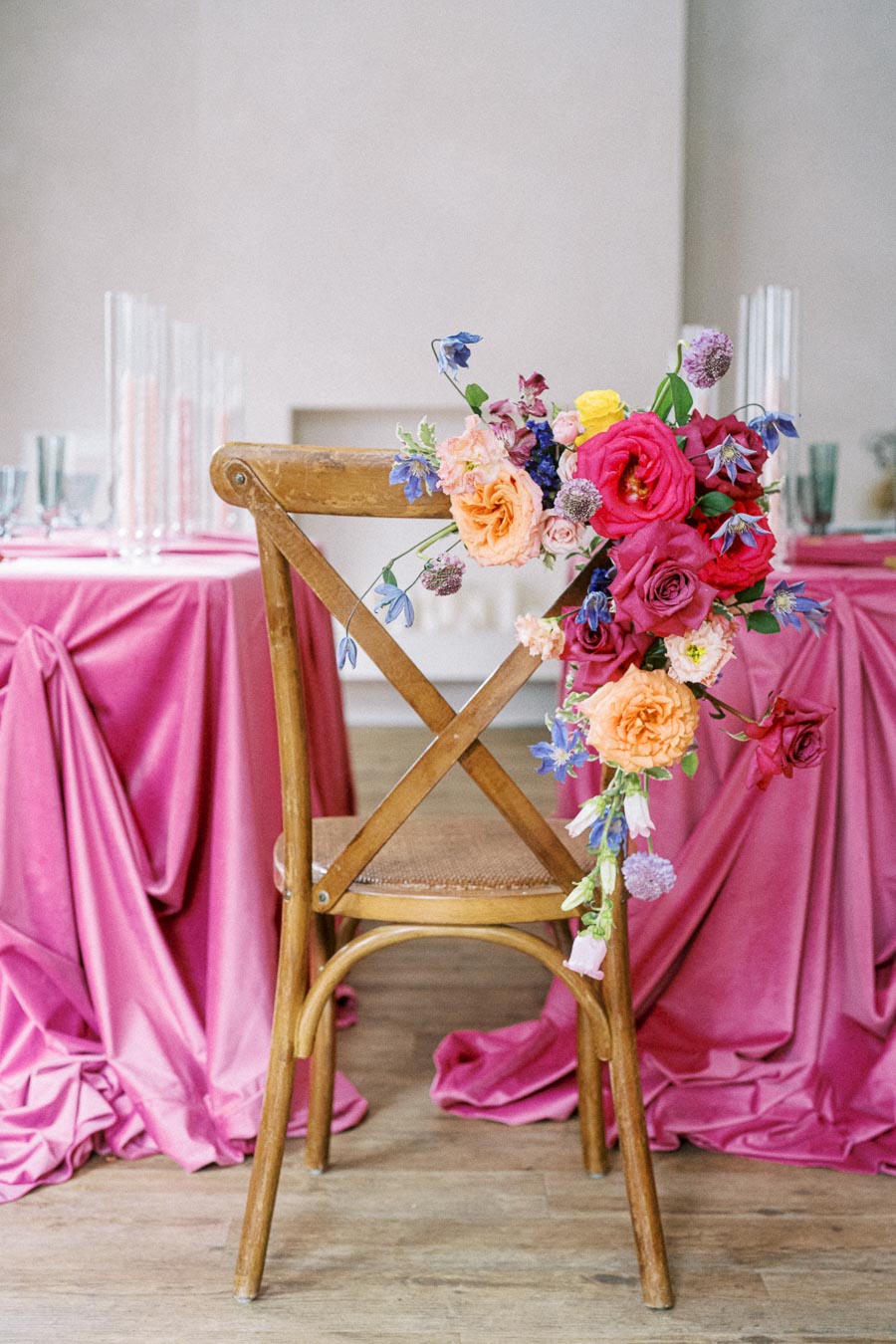 Elegant wedding reception chair adorned with a vibrant bouquet of flowers, set against a pink draped tablecloth, creating a romantic and colorful decor ambiance.