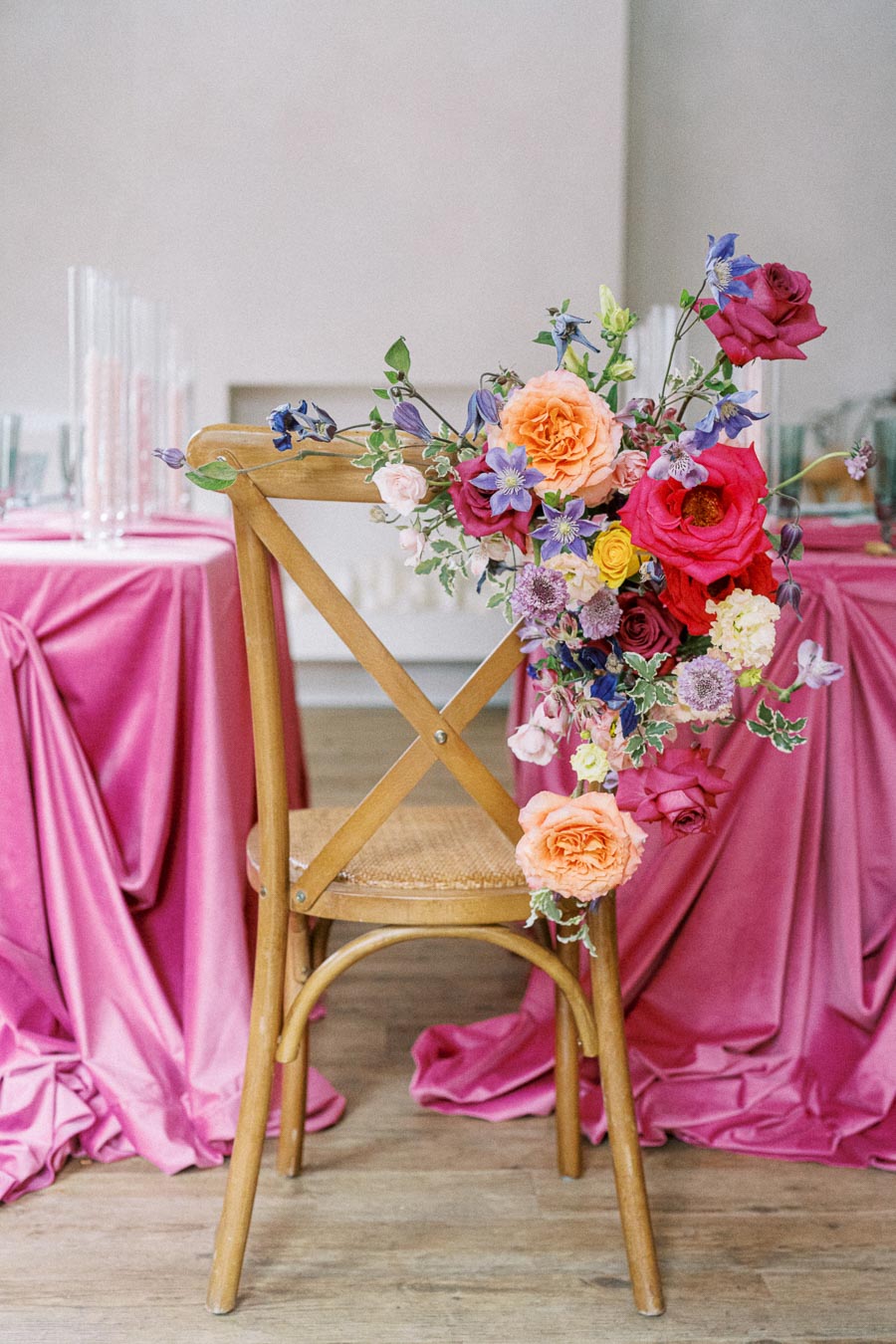 Wooden chair with colorful floral arrangement against a pink tablecloth backdrop, perfect for a spring or summer wedding decor setting.