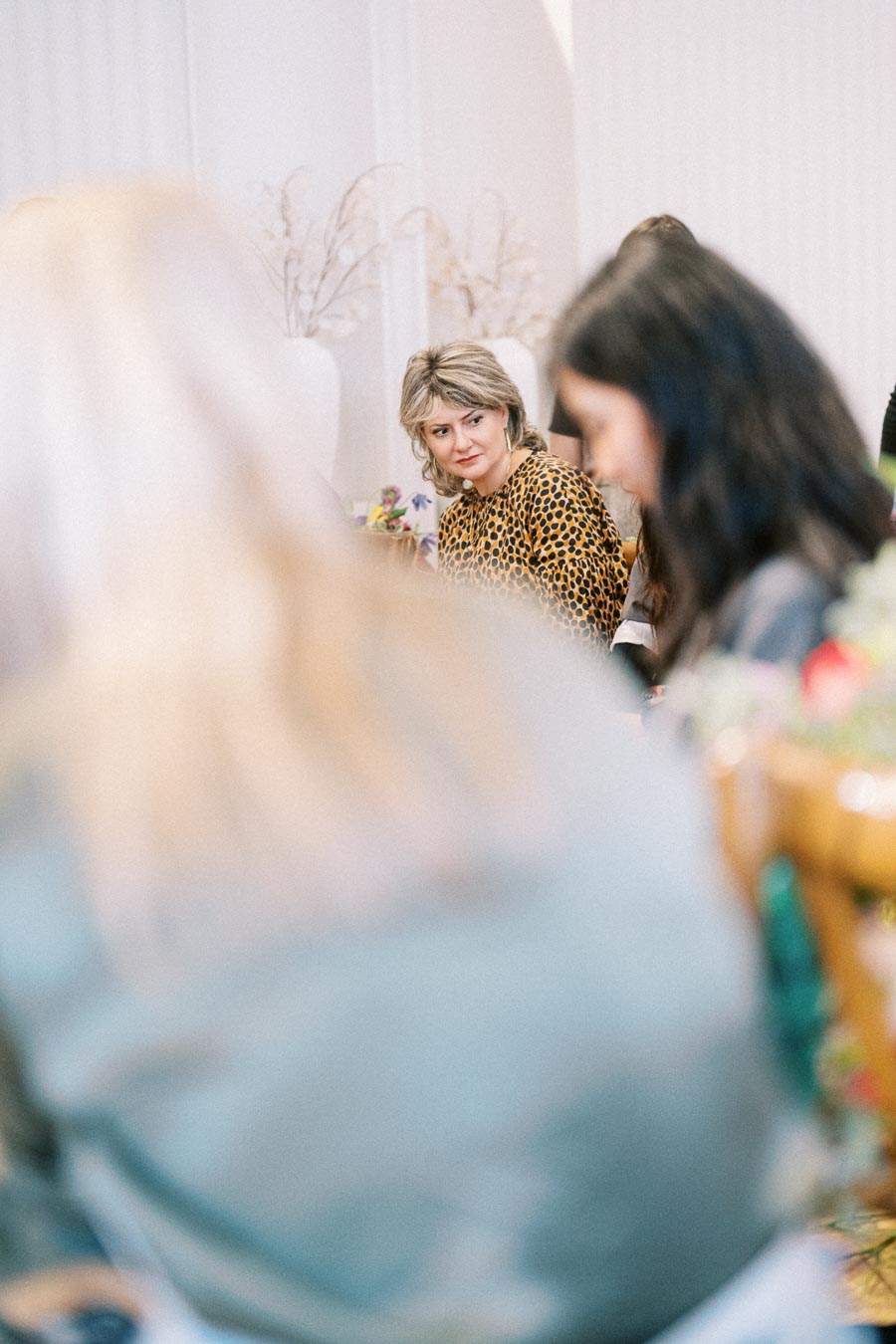 Woman in a leopard print top attending a meeting, surrounded by blurred participants, in a bright, well-lit room setting.