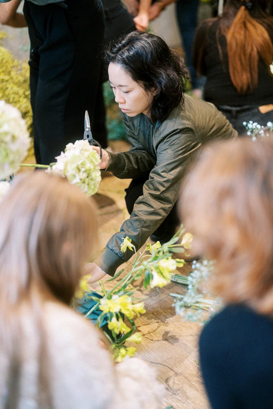 Person arranging flowers in a workshop setting, holding a pair of scissors and focusing on floral design.