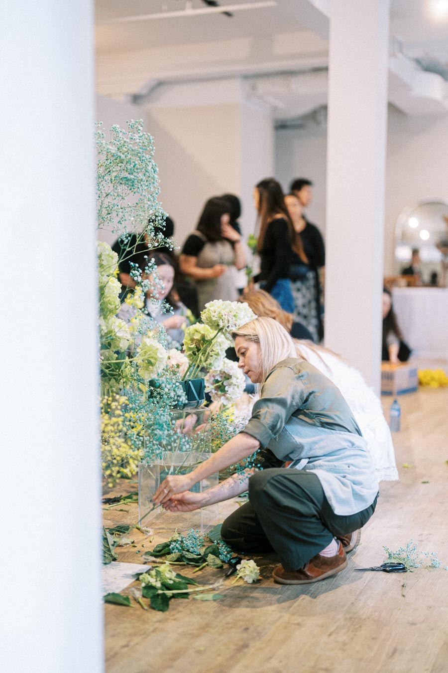 Florist arranging flowers in a creative workshop setting, surrounded by people observing and learning floral design techniques.
