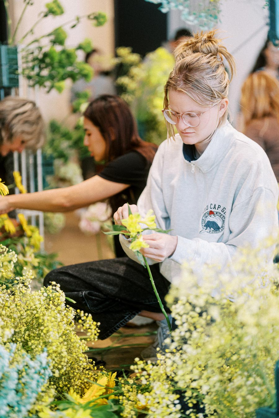 Person arranging vibrant yellow flowers in a garden setting, with focus and care in a creative workshop environment.