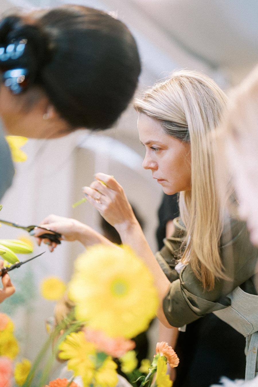 Two women concentrating on arranging colorful flowers, using scissors to trim stems in a floral workshop setting.