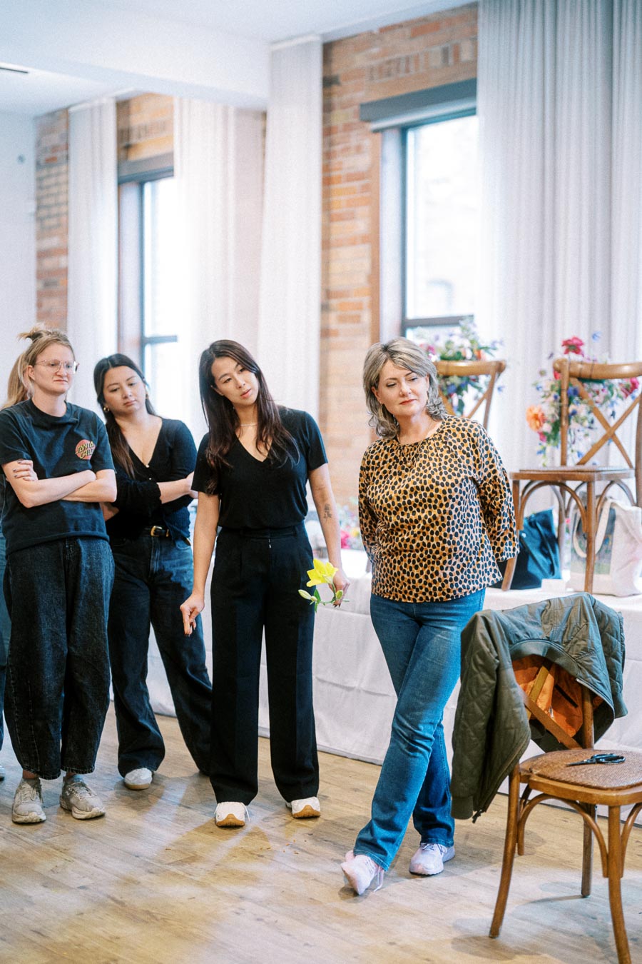 Group of women engaging in a creative workshop in a well-lit room, with flowers and chairs in the background.