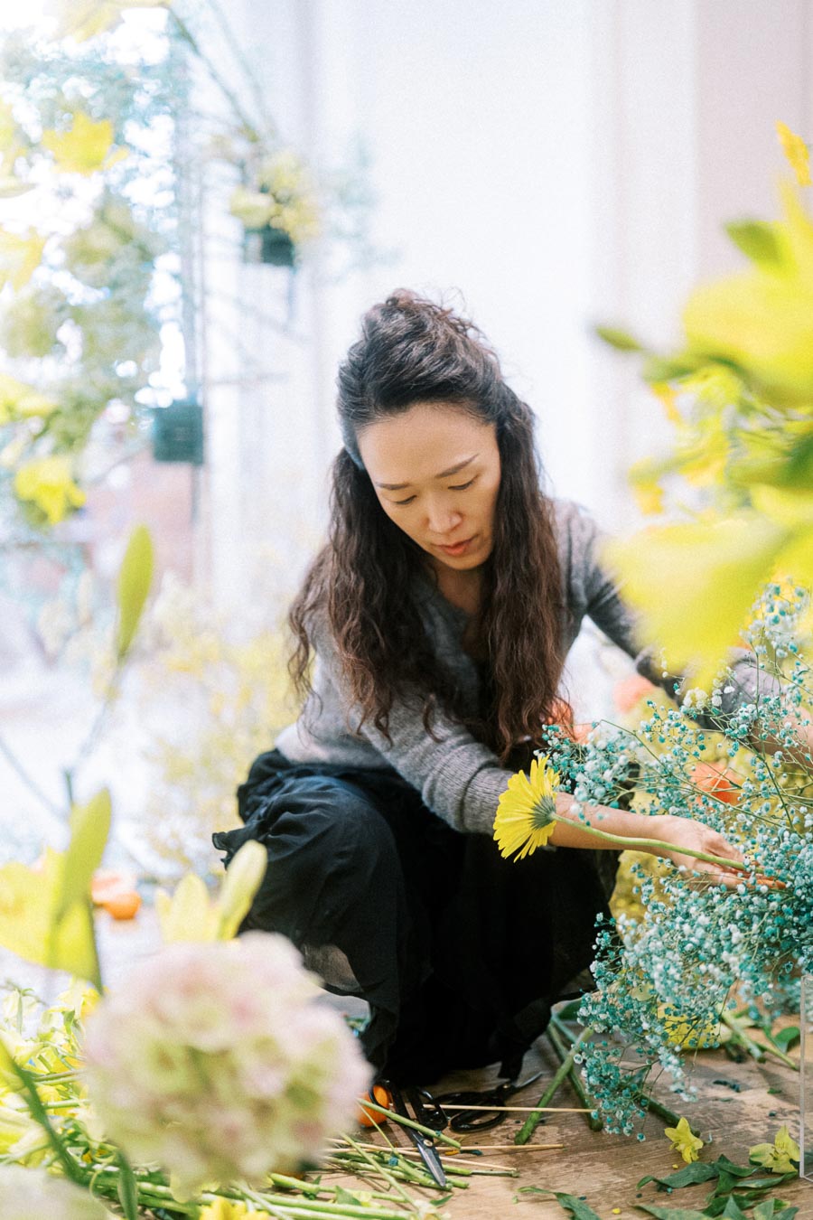 Florist arranging colorful flowers in a bright workshop, surrounded by yellow and blue blossoms.