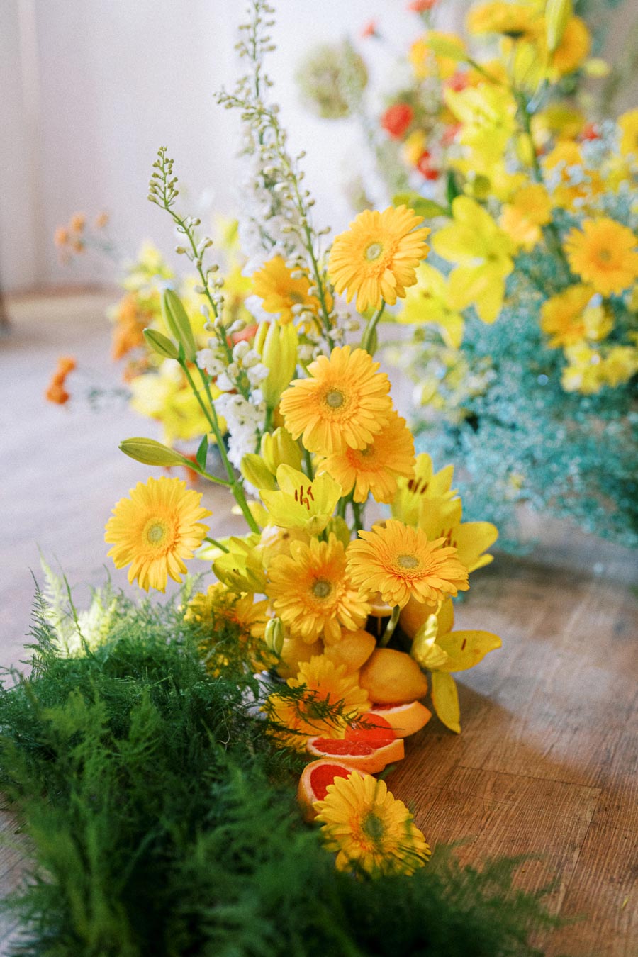 Vibrant arrangement of yellow flowers and citrus fruits with lush green foliage on a wooden table surface, showcasing a fresh and lively floral centerpiece ideal for spring decor inspiration.