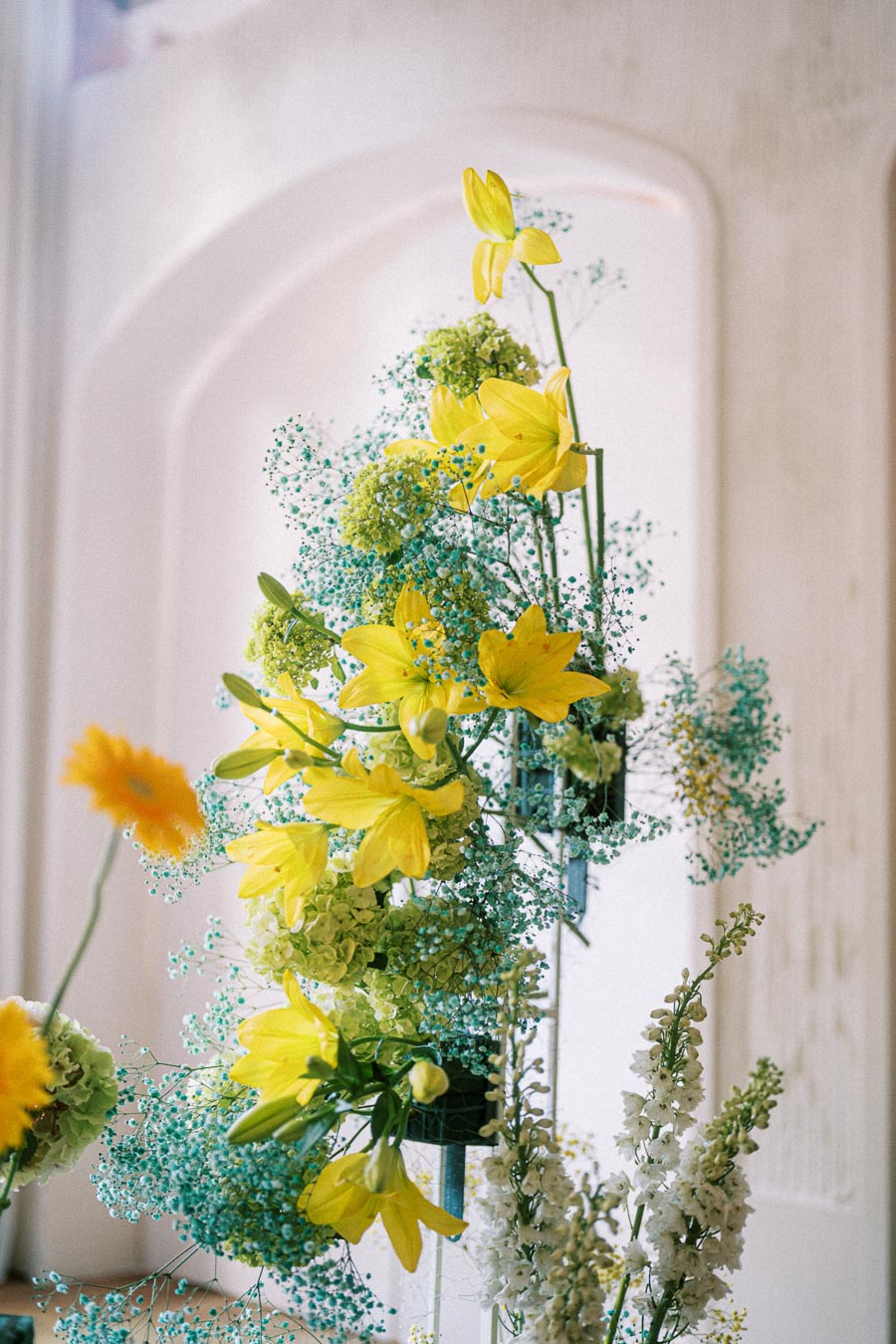 Bright floral arrangement featuring yellow lilies, green hydrangeas, and delicate blue baby's breath against a soft, neutral background, perfect for weddings or spring events.