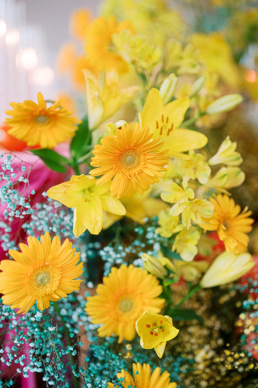 Beautiful arrangement of vibrant yellow flowers, including gerberas and lilies, with accents of small blue blossoms, showcasing a lively and colorful floral display.
