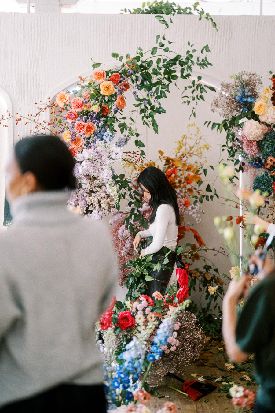 Floral artist arranging a vibrant display of colorful flowers and greenery at an event, featuring roses, hydrangeas, and various blossoms intertwined with leaves.