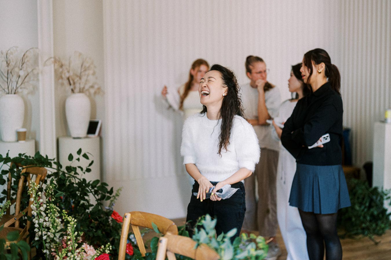 A group of people enjoying a light-hearted moment in a well-decorated room with indoor plants and stylish vases in the background.