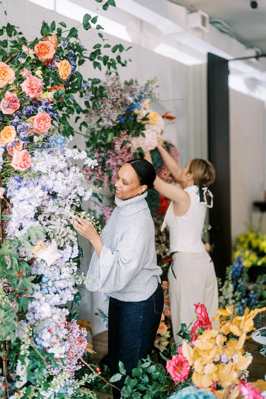 Women arranging colorful floral displays in a modern workshop setting.