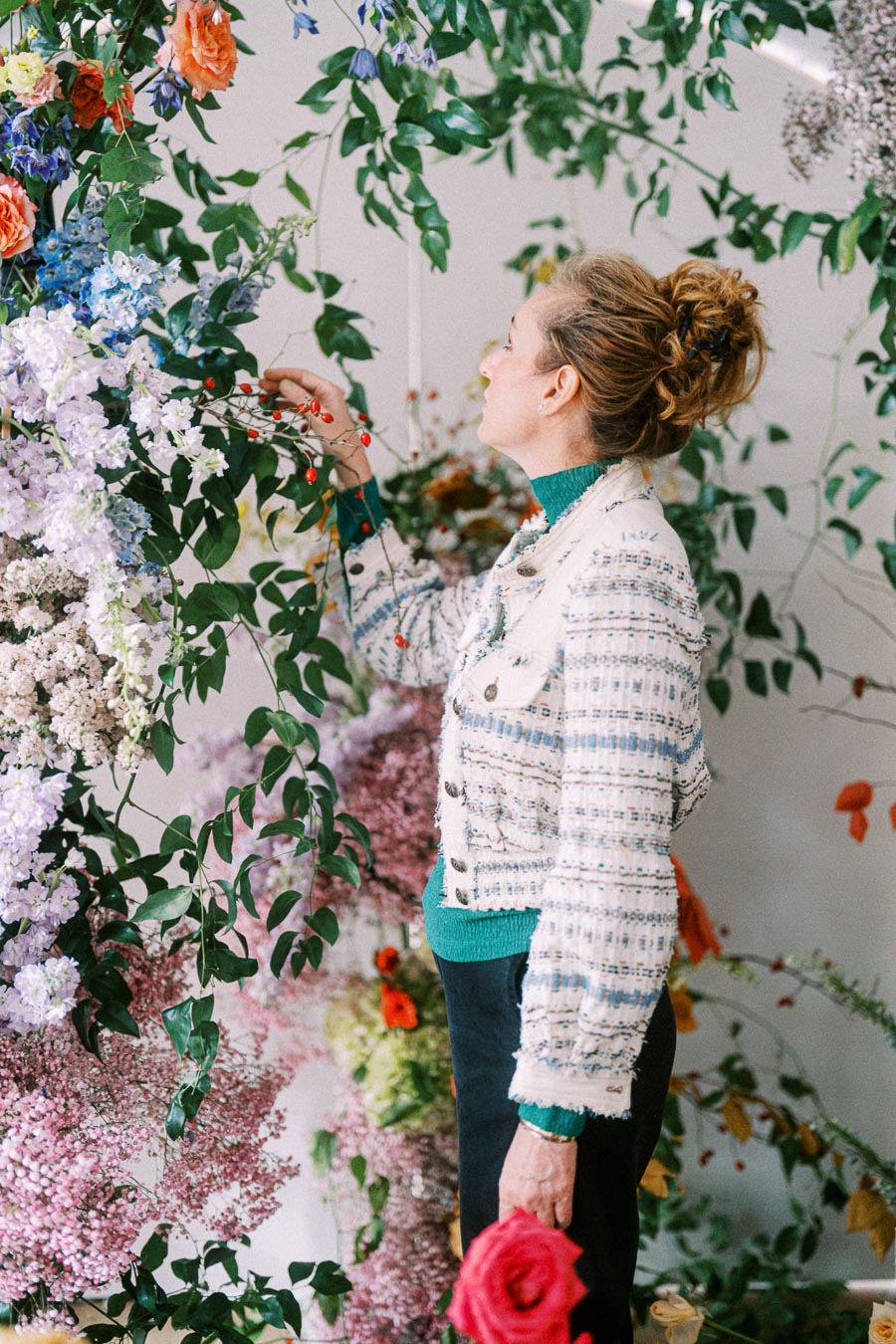A woman arranging a vibrant floral display with various colorful flowers and lush green leaves indoors.