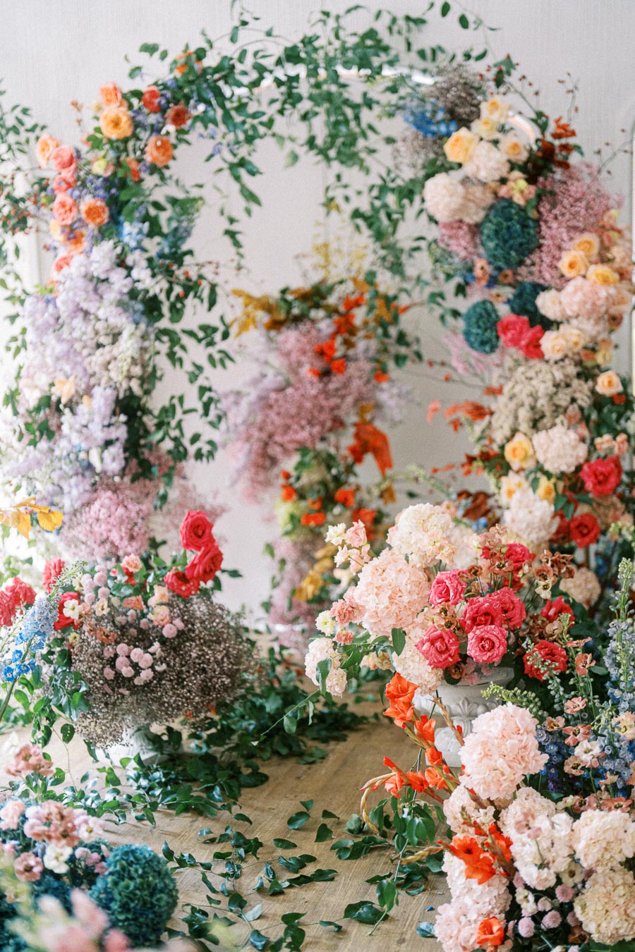 Vibrant floral arrangement featuring lush greenery and assorted colorful flowers, including roses and peonies, set against a light background. Ideal for wedding or event decor inspiration.