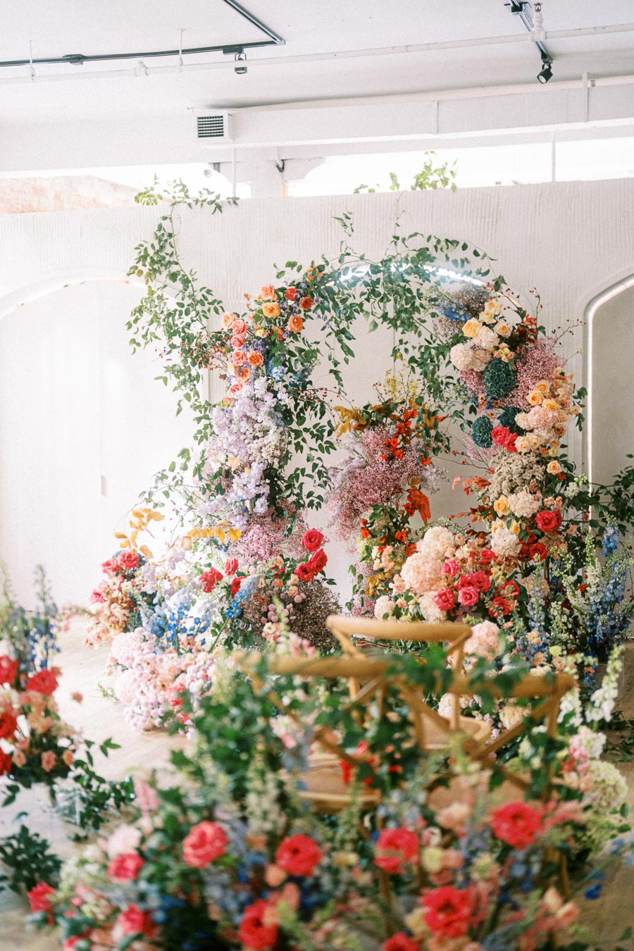 Floral arch display with colorful flowers including roses, peonies, and greenery in a bright, modern event space.