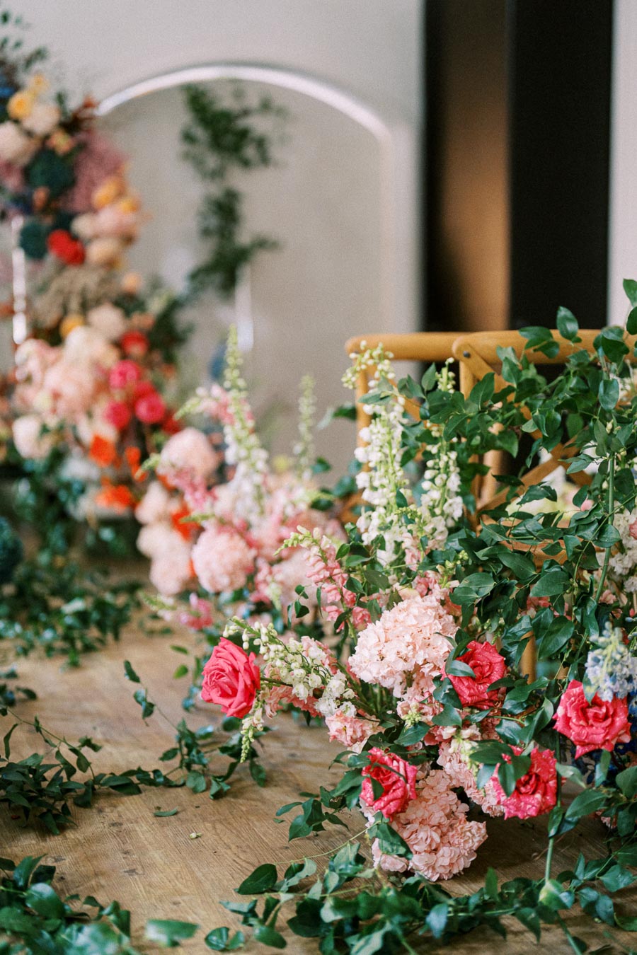 Elegant floral arrangement with pink roses and lush greenery on a wooden floor, creating a romantic wedding aisle decor.