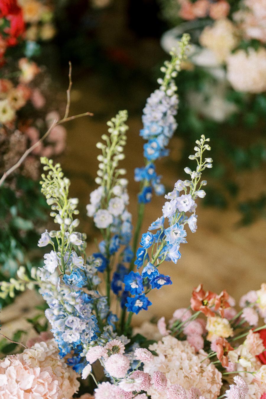 A vibrant floral arrangement featuring tall blue delphinium flowers surrounded by soft pink and peach blossoms. Perfect for adding natural elegance to a garden-themed event or wedding decor.
