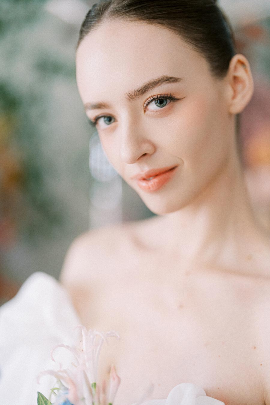 Elegant portrait of a woman with a serene expression, holding delicate white flowers. The soft focus background adds a dreamy and ethereal quality, emphasizing the subject's natural beauty and calm demeanor. Perfect for themes of grace, beauty, and tranquility.