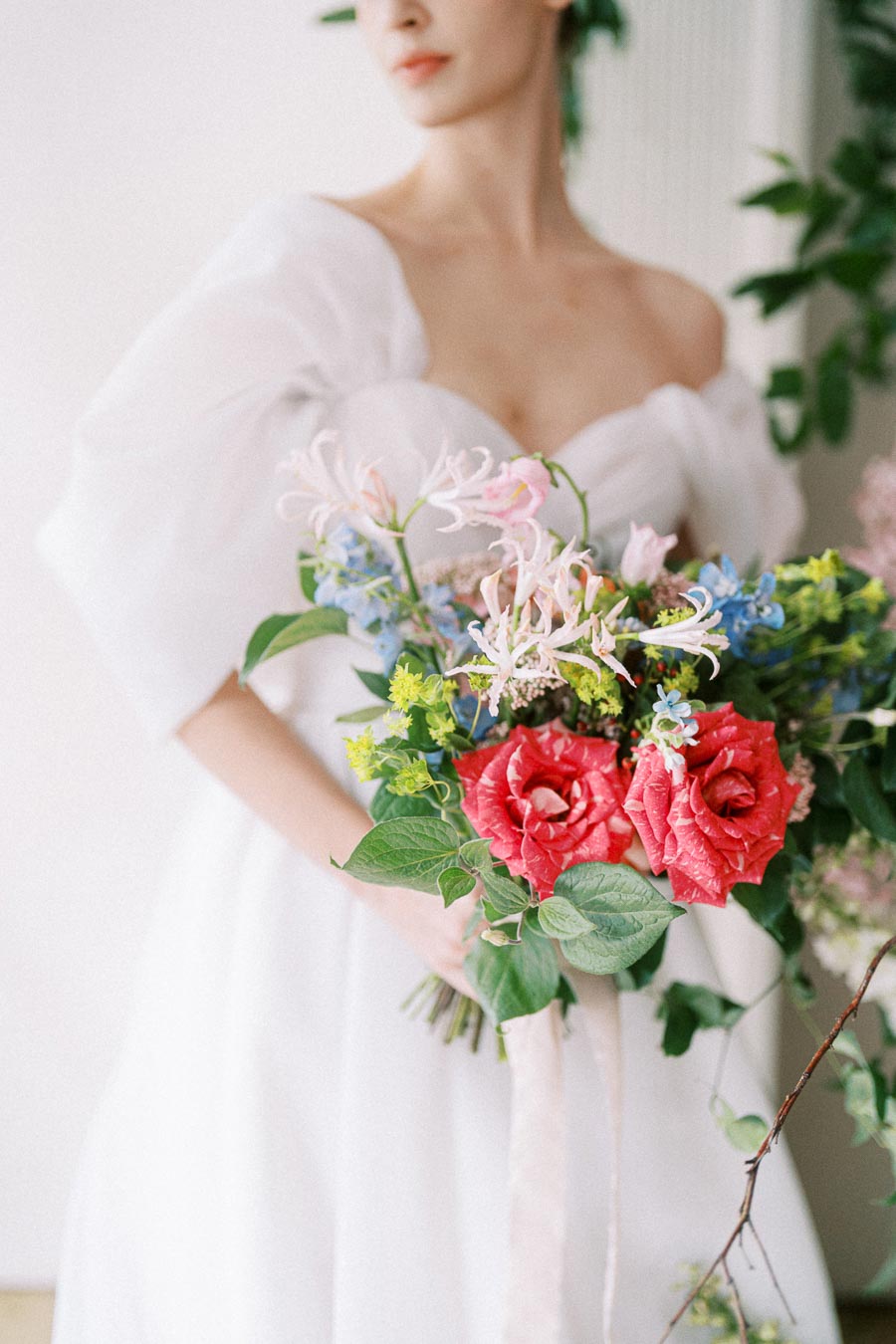 A bride in a white dress holding a vibrant floral bouquet with red roses and blue, pink, and yellow flowers.