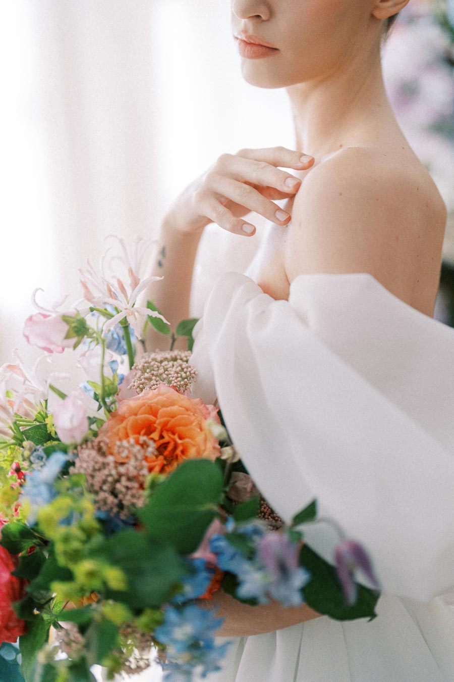 Elegant bride holding a vibrant bouquet of colorful flowers, showcasing intricate wedding dress details.