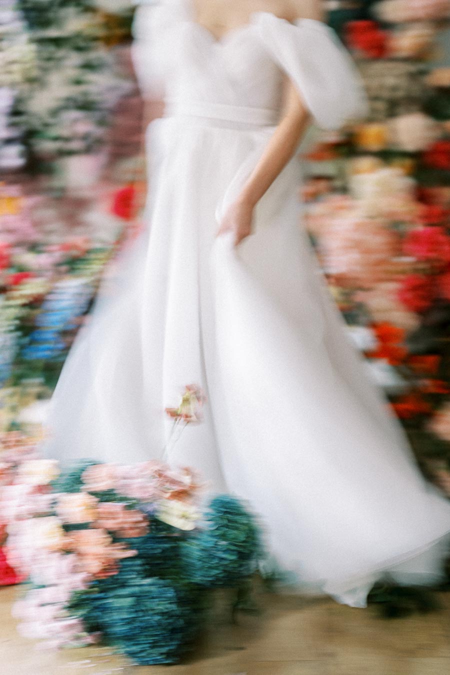 Blurred image of a woman in an elegant white wedding dress, surrounded by colorful flowers, creating an artistic and dreamy effect.