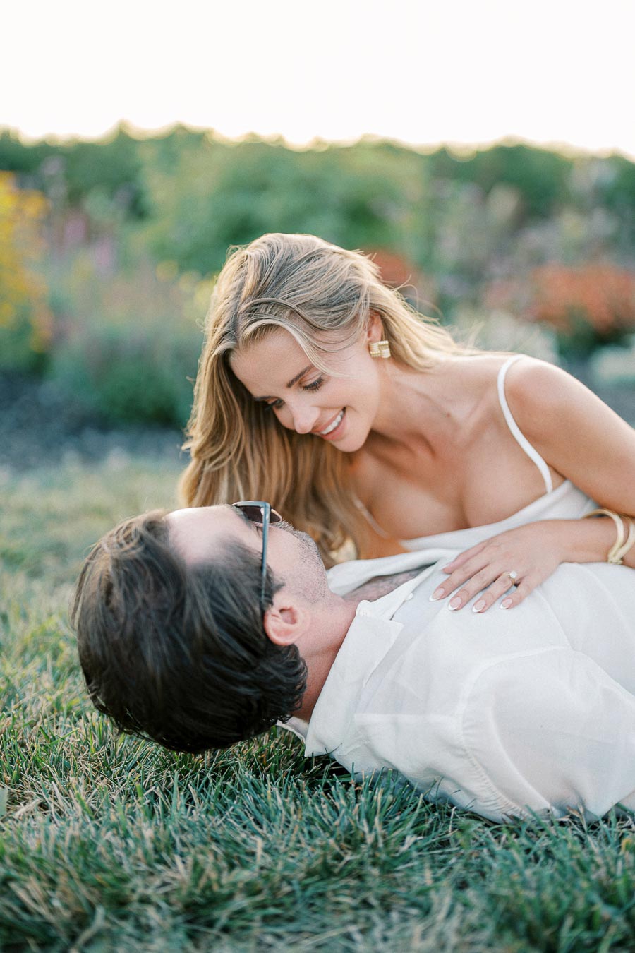 A couple lying on grass lovingly gazing at each other in a serene garden setting.