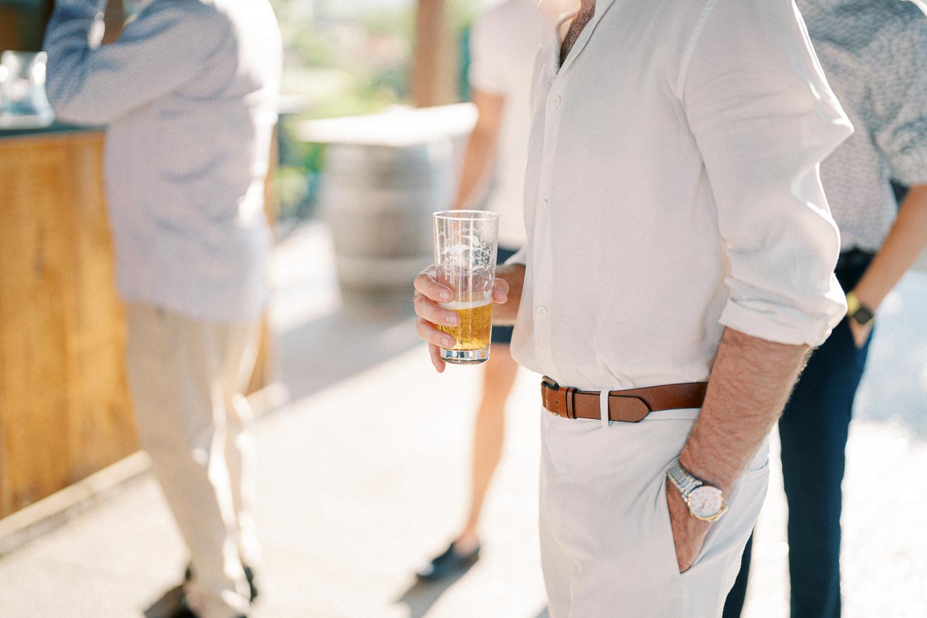 A person in a white shirt holding a glass of beer at an outdoor event.
