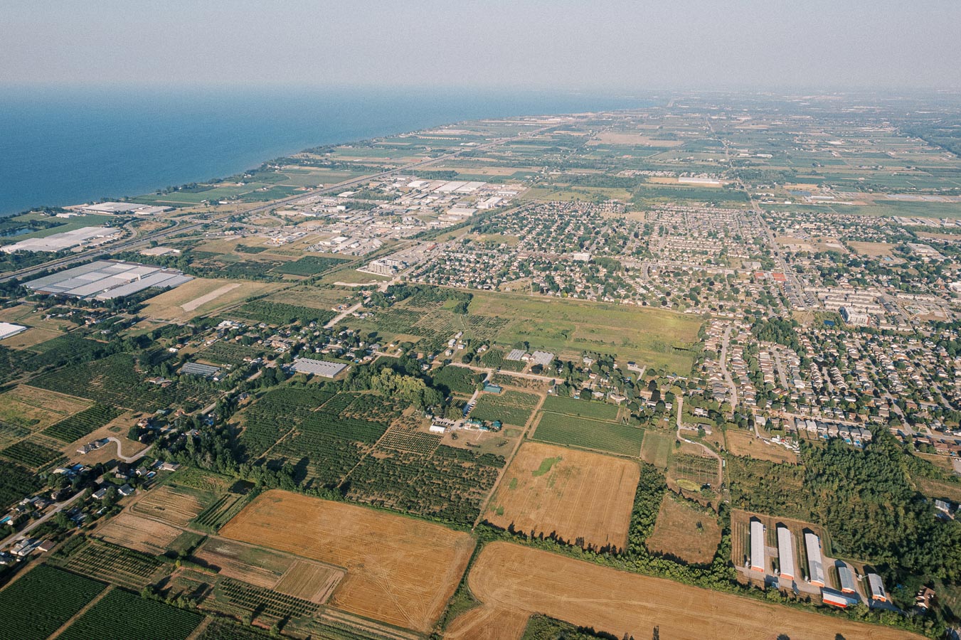 Aerial view of a rural landscape with agricultural fields, residential areas, and a distant coastline under a clear sky.