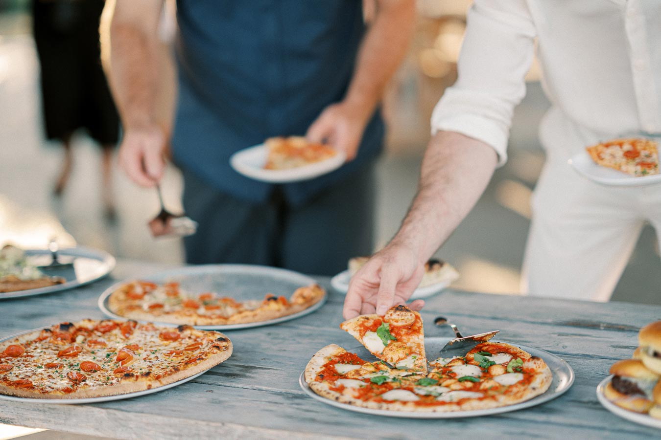 Group of people enjoying a selection of gourmet pizzas at an outdoor gathering.