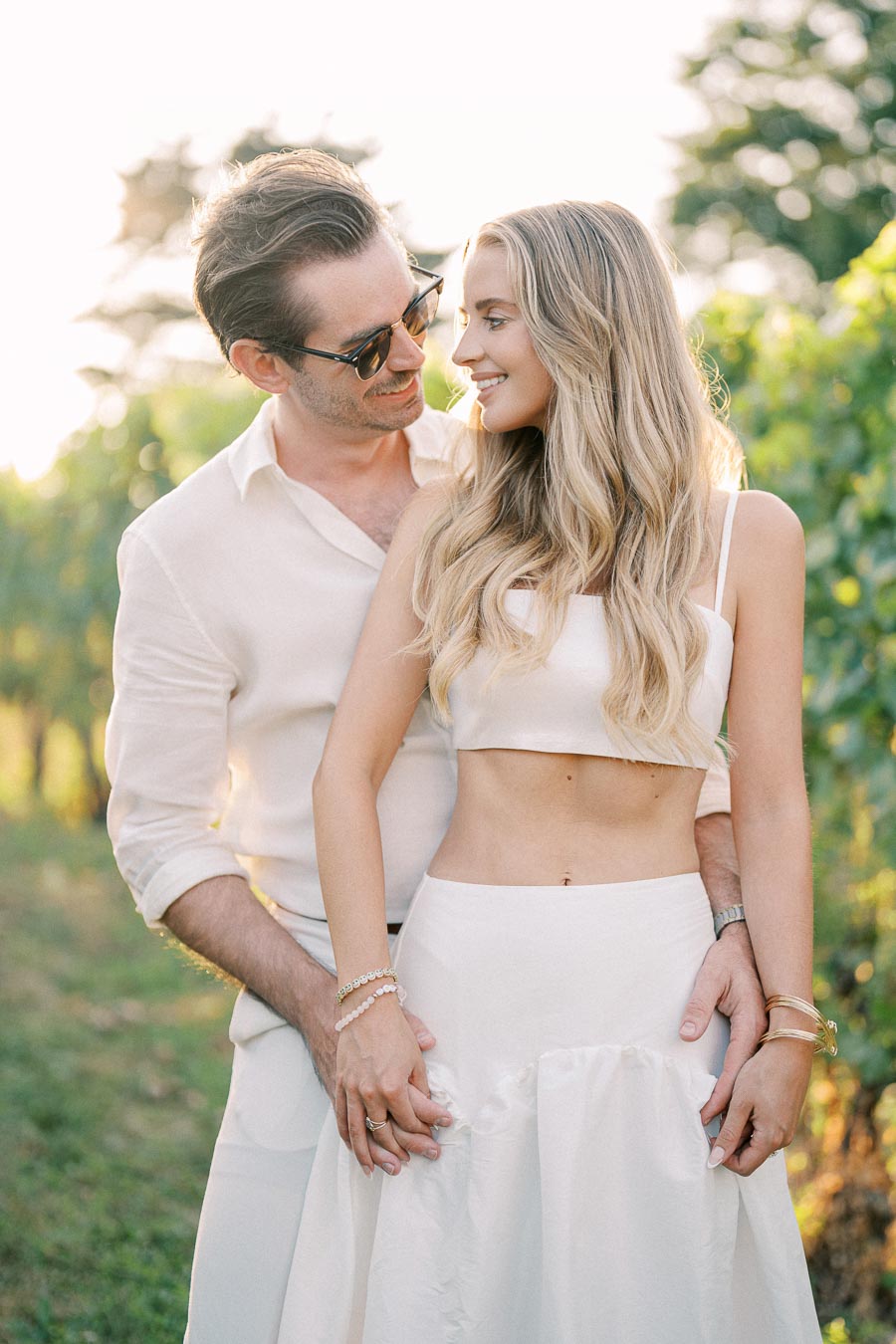 A couple embraces affectionately in a sunlit vineyard, dressed in light, summer attire, embodying romance and warmth.