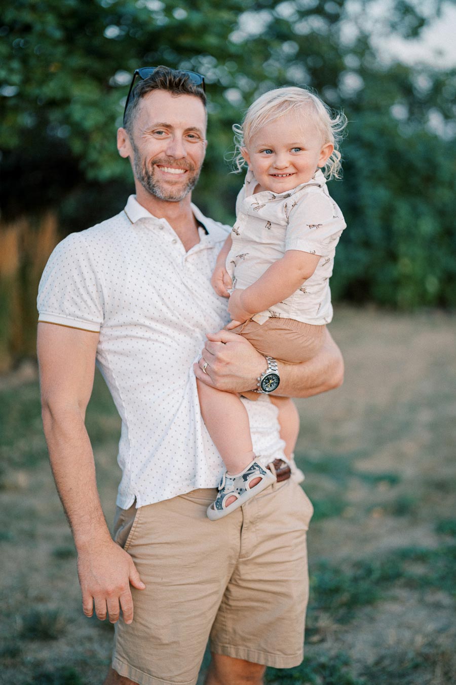 Father smiling and holding his young child outdoors in a park.
