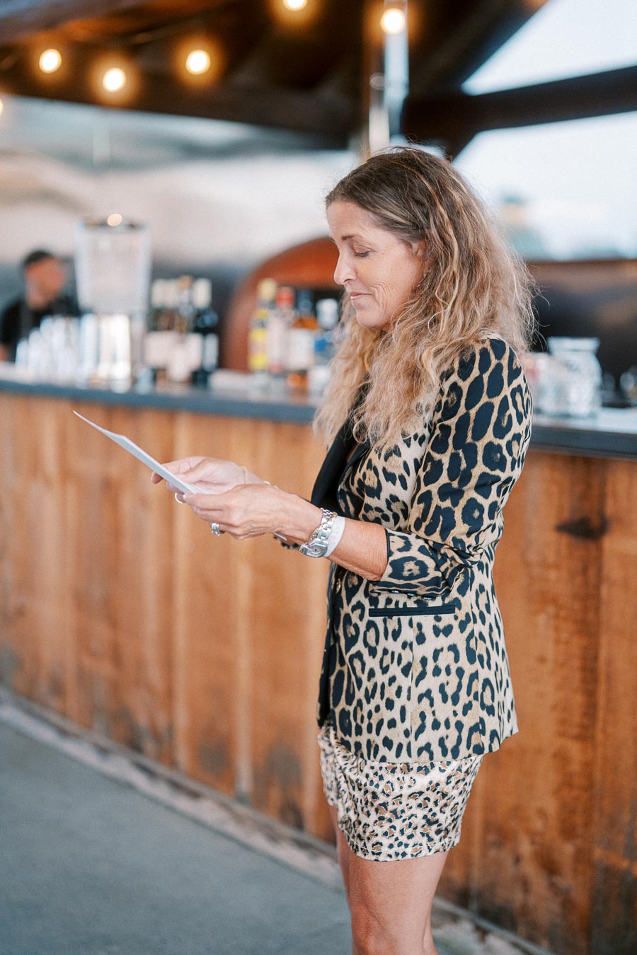 A woman in a stylish leopard print outfit reads a paper in a warmly lit bar setting.