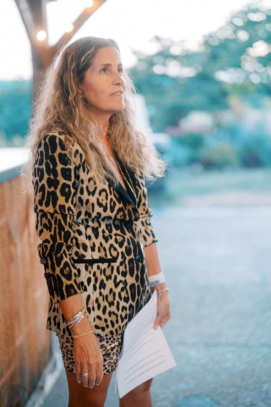 Woman in leopard print suit holding papers, looking thoughtful outdoors.